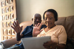 A senior couple wave at family members on a tablet device because keeping in touch with loved ones is an important way to reduce depression in older adults.