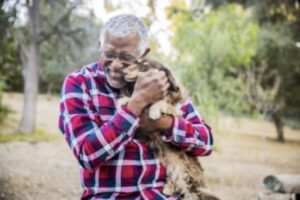 An older man smiles as he hugs his dog, living his best life in spite of a chronic health condition.