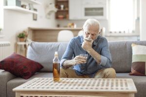 An older man struggling with substance abuse in seniors gazes thoughtfully into his glass of whiskey.