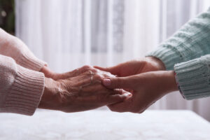 An older woman’s hands are held by a younger woman’s hands, representing the need for promoting mental health in older loved ones.