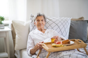 An older woman receiving comfort care at end of life sits in bed with a tray of food.