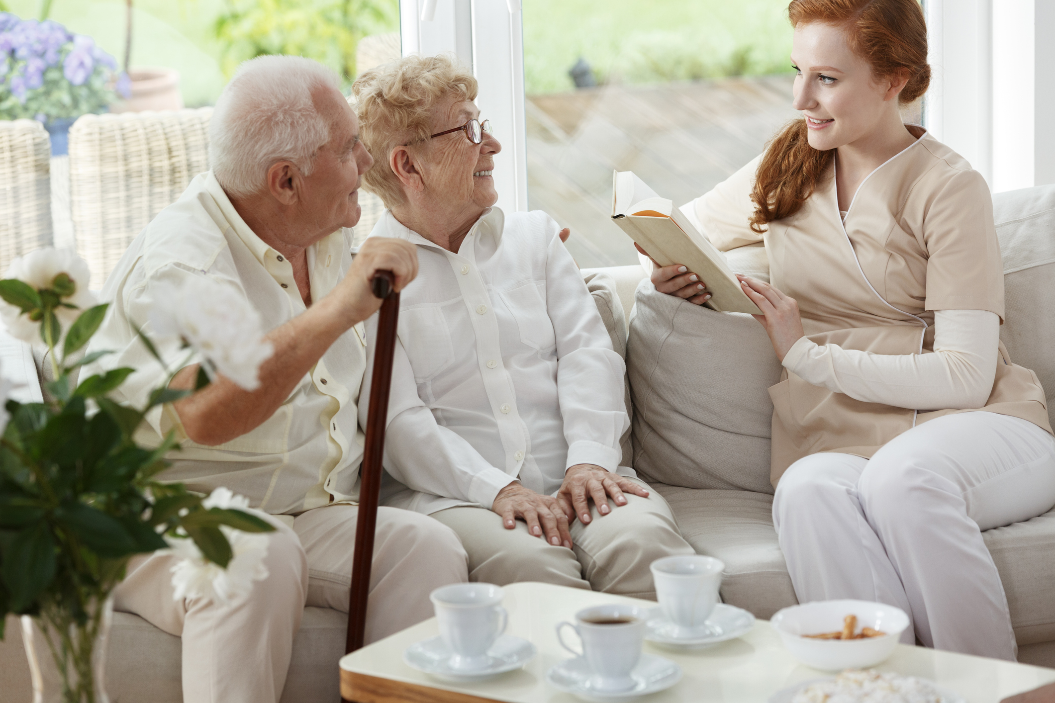 Caregiver reading a book to a happy senior couple
