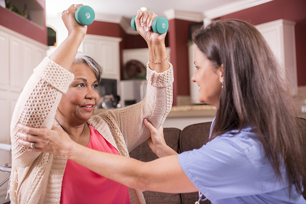 Friendly caregiver helping senior woman with exercises