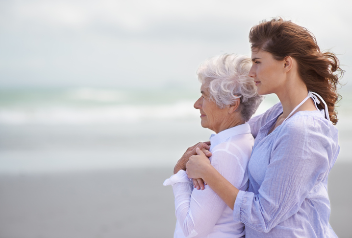 A woman who knows how to process the emotions of caring for someone with dementia hugs her mother as they gaze out at the ocean.