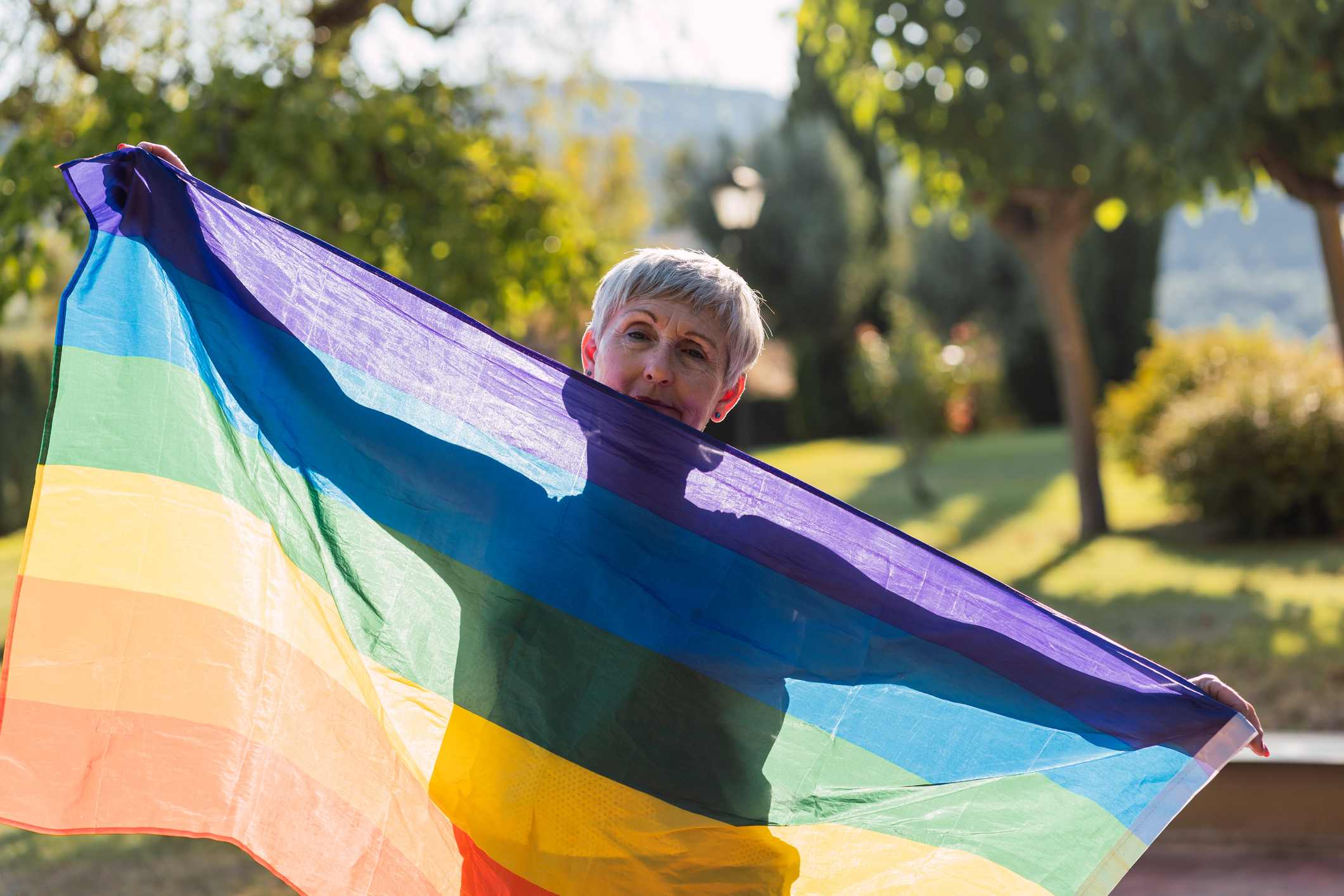 A woman who is part of the community of LGBTQ+ seniors holds up a rainbow flag.