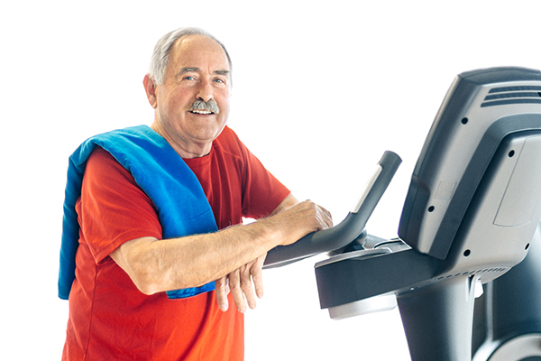 An older man who has learned about the link between exercise and Parkinson’s smiles as he leans on a treadmill.