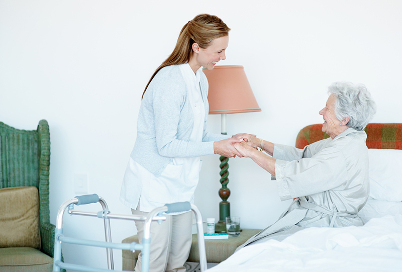 A caregiver utilizes techniques for safe lifting and transfers at home as she helps an older woman get out of bed.
