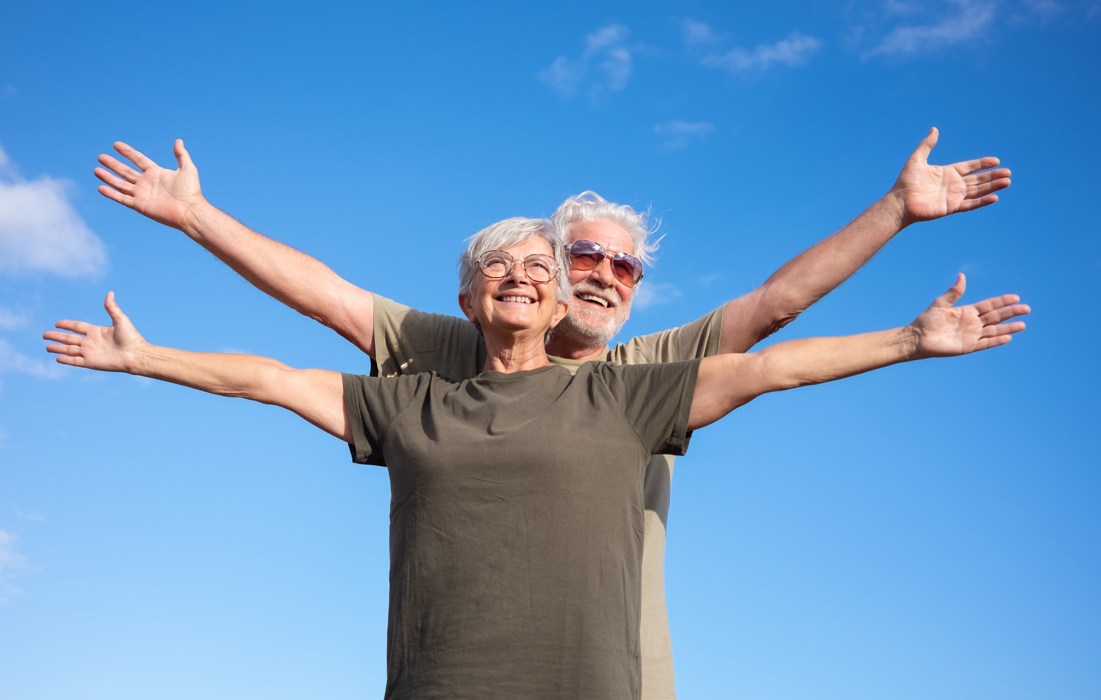 Two older adults spread their arms wide against a blue sky, symbolizing their freedom from chronic pain.