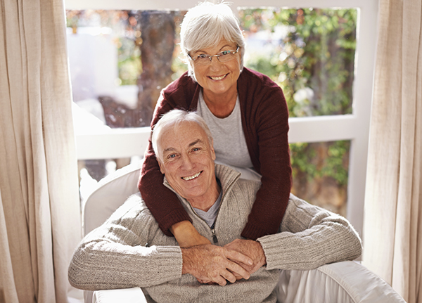 An older couple receiving home care help to age at home smile in front of a window.