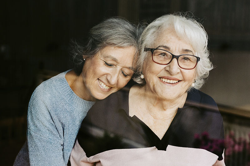 A woman who is overcoming the challenges of dementia care smiles as she hugs her elderly mother.