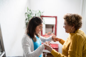 An older woman experiencing the challenges of MS holds the hands of her caregiver.