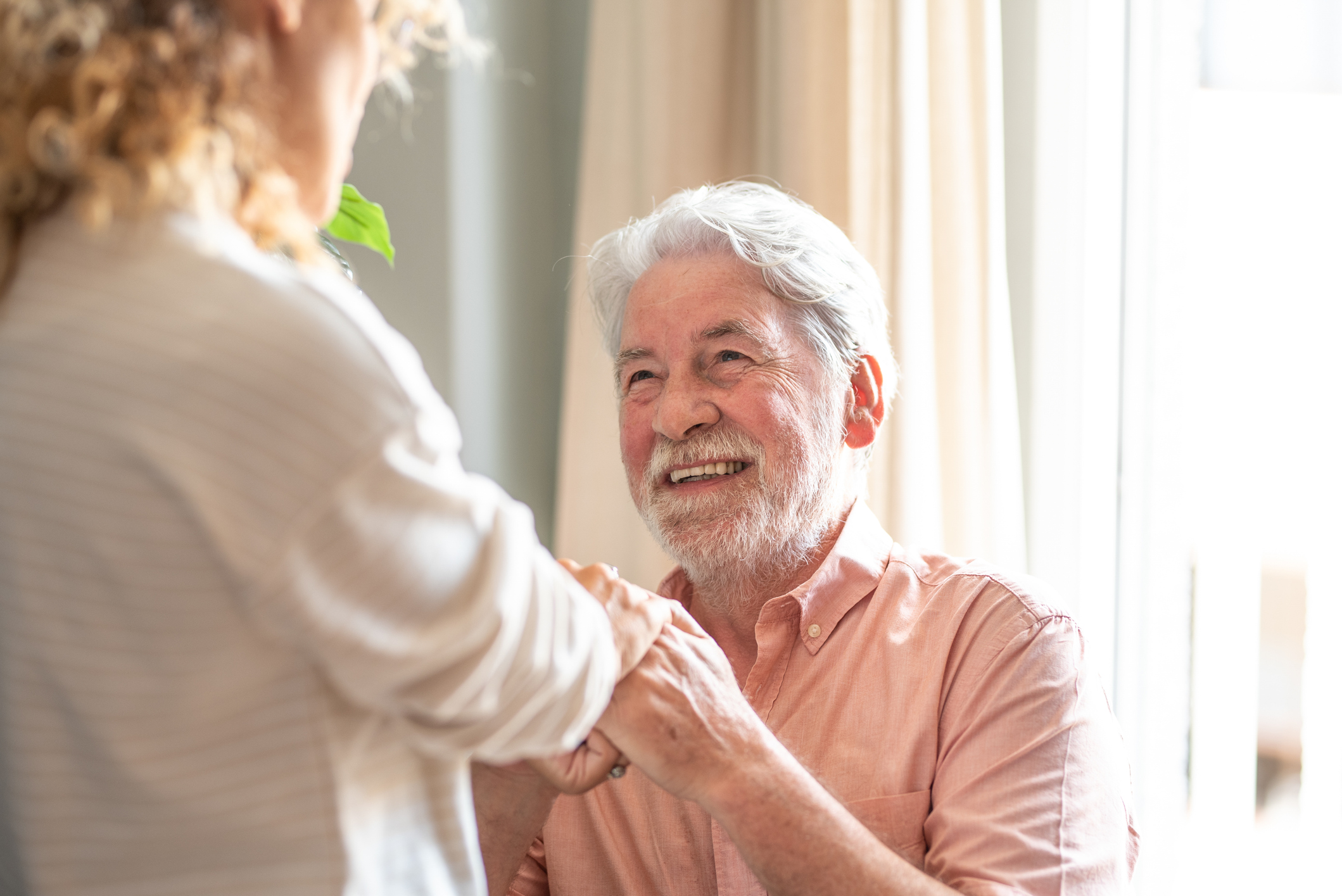 A caregiver holds the hands of an older man who has just come home after a stroke.
