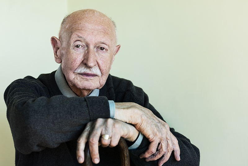 A man whose caregiver prioritizes helping seniors stay independent leans confidently on his cane.