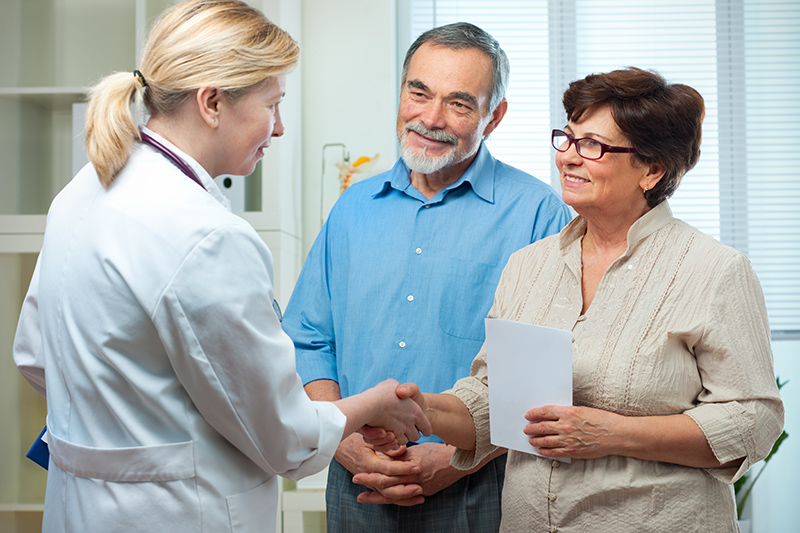 A woman who is supporting a senior at medical appointments shakes the hand of her husband’s doctor.