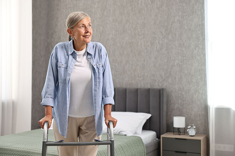 A woman stands with the help of a walker as she faces hip replacement recovery at home.