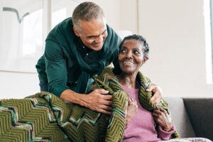 A senior man covers his wife with a cozy blanket as he strives to avoid common Alzheimer’s caregiver mistakes.