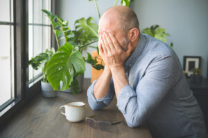 A man struggles with recognizing PTSD symptoms in seniors and rests his head in his hands.